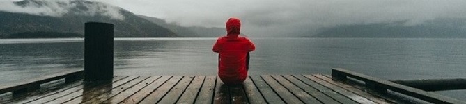 Back view of someone sitting on a jetty looking out to the water