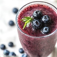 Glass of blueberry smoothie with some of the fruits in the background