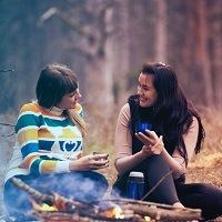 Two friends chat around a camp fire