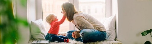 Happy mother and child facing each other on a sunlit window seat