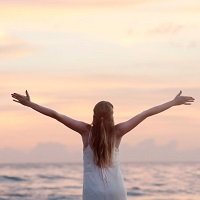 Back view of woman with arms outstretched facing the ocean