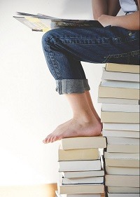 Legs and feet of someone sitting on a stack of books studying