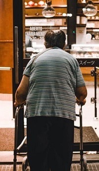 Back shot of a man with a walking frame going into a shop