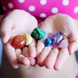 A girl holds her palms open to display a collection on vividly-coloured gemstones