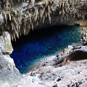 Underground mineral producing cave opening shows deep blue water pool