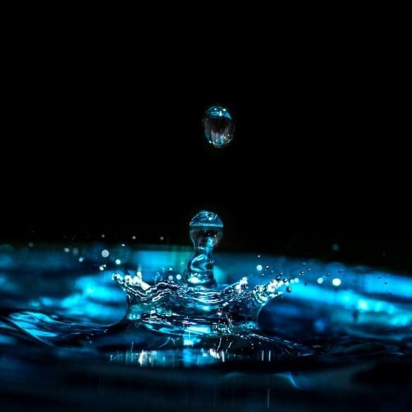 Drops of water in a small blue pool against a black background